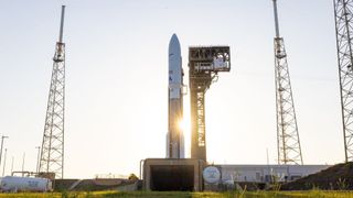 The sun shines behind a white and brown Atlas V rocket carrying Amazon's Kuiper 1 satellites for an April 29, 2025 launch.