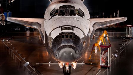 a winged back and white orbiter standing on its landing gear is seen on museum display