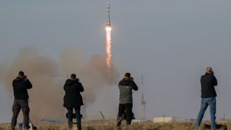 A Russian Soyuz roket launches into space with four photographers tracking it in the foreground.