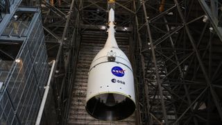 A white cone with NASA and ESA logos is lowered inside a large warehouse bay.
